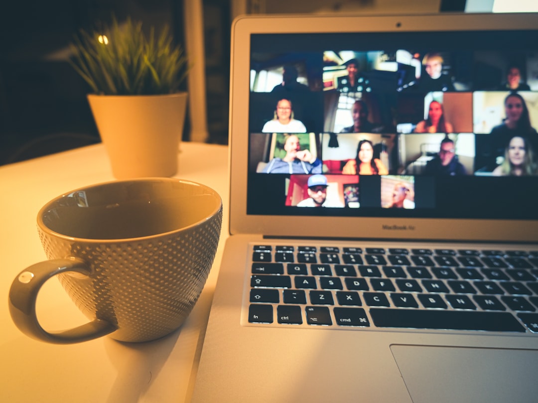 Laptop showing a video conference grid on the screen, with a mug and potted plant on the desk.