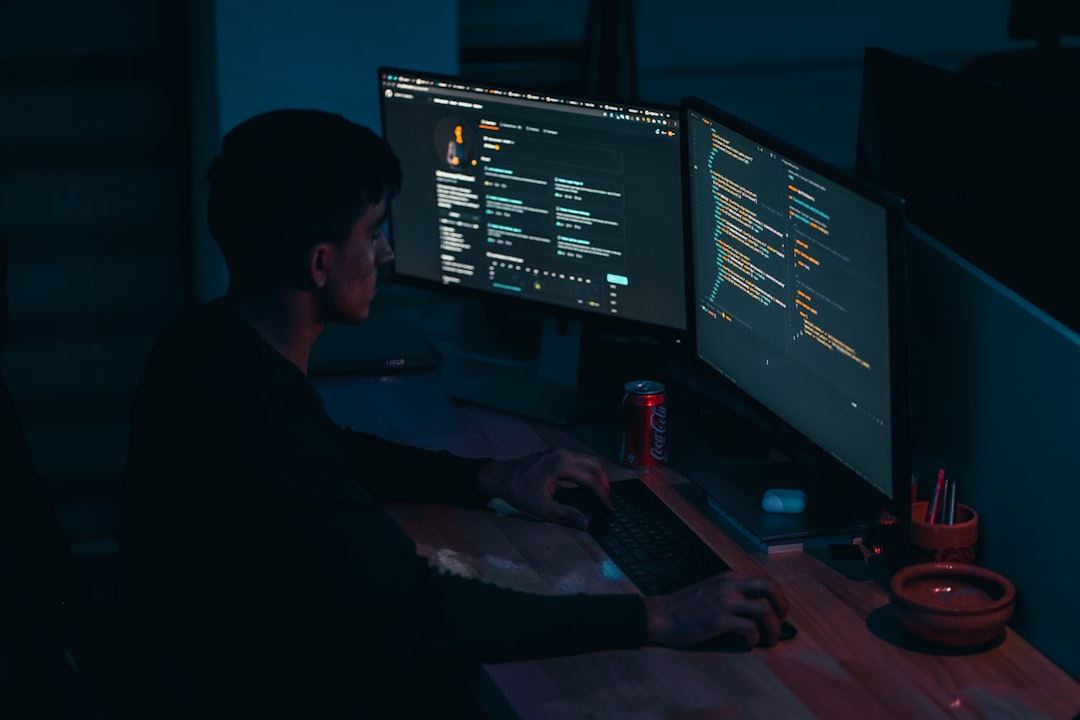 Person coding at a desk with two monitors displaying code in a dim blue-lit room, a Coca‑Cola can nearby on the desk.