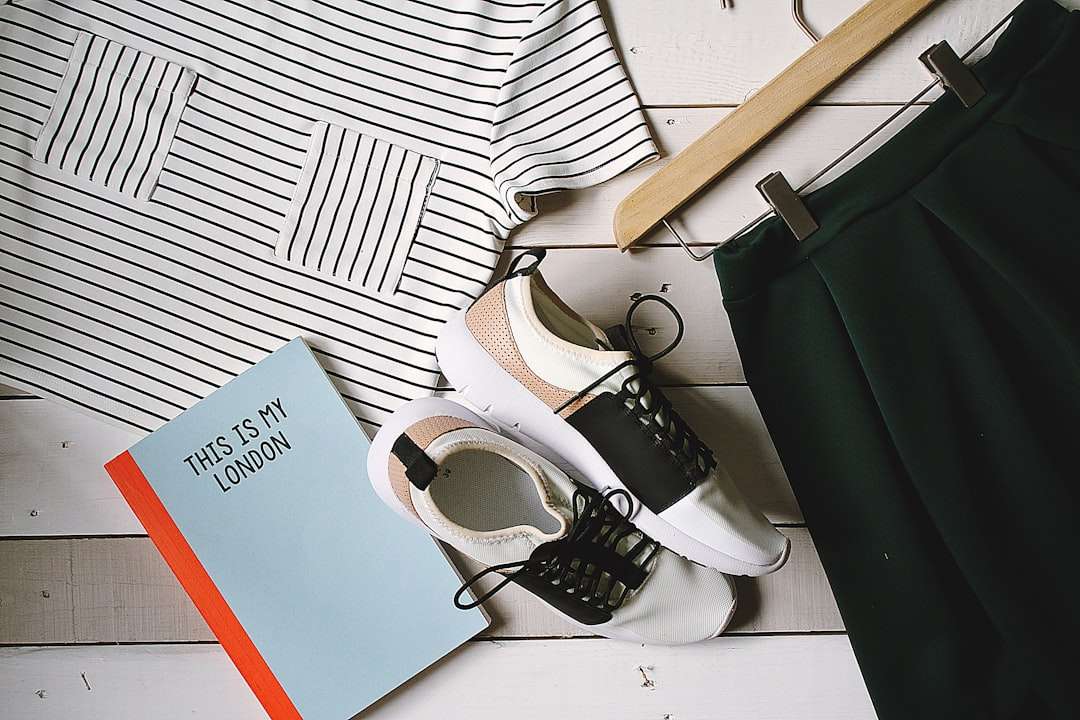 Flat lay: striped T-shirt, white sneakers with beige accents, dark trousers on hangers, and a blue book titled 'This Is My London'.