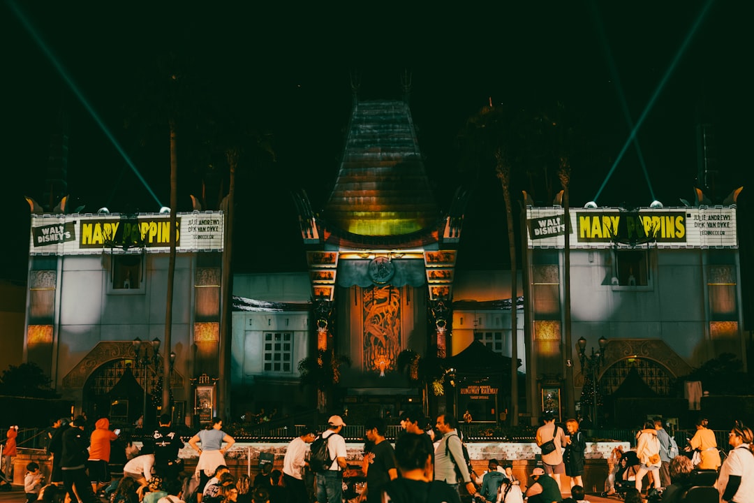 Nighttime view of a large theater facade lit in orange and teal, with a crowd gathered in front for a Mary Poppins show.