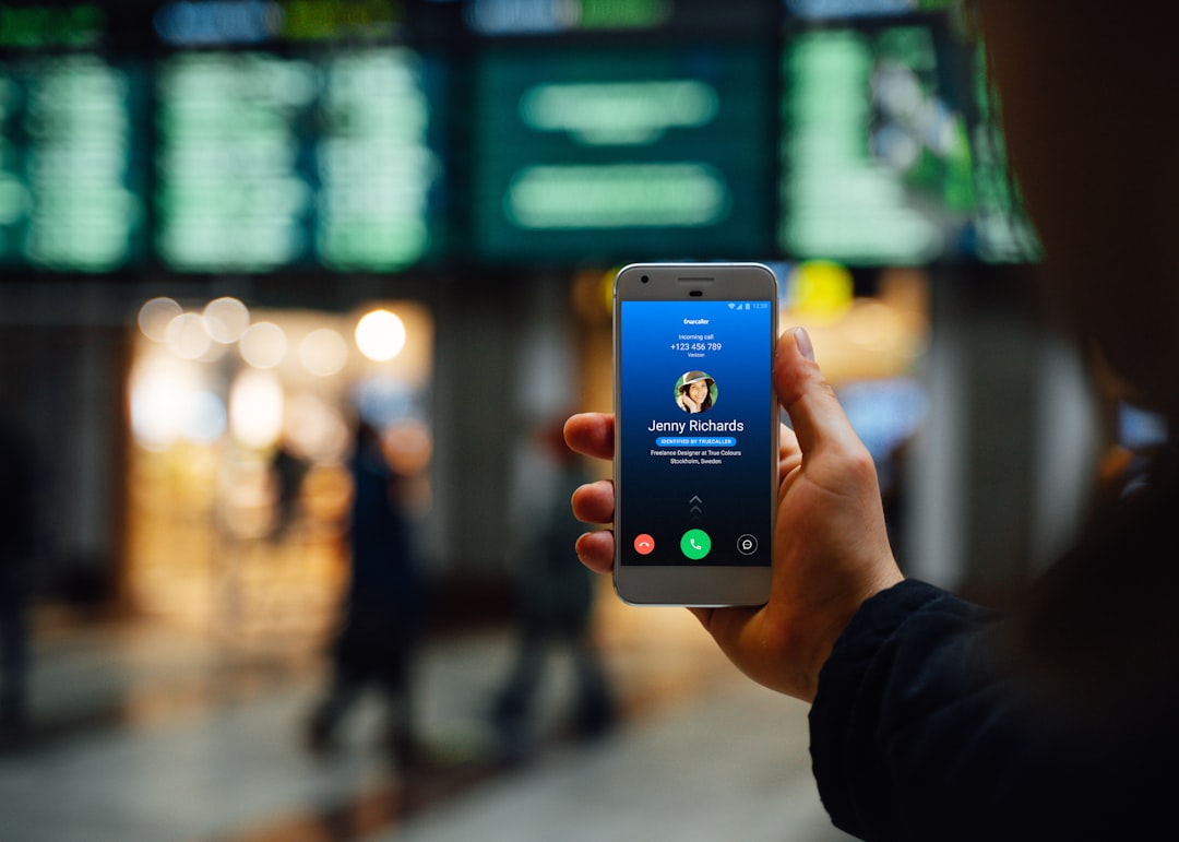 Person holding a smartphone showing a video call screen with the name Jenny Richards in a busy terminal.