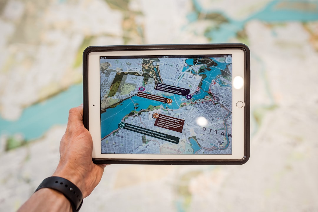 Hand holding a tablet displaying a colorful city map with numbered markers and labels.