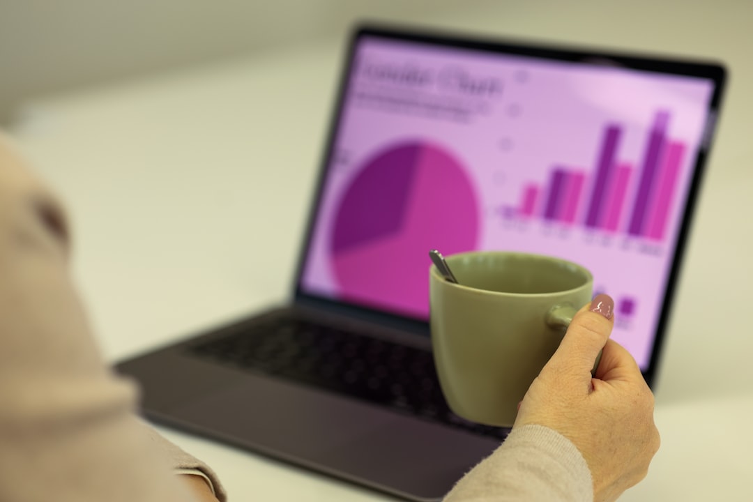 Person holds a mug in front of a laptop displaying pink and purple charts (pie chart and bar graph).