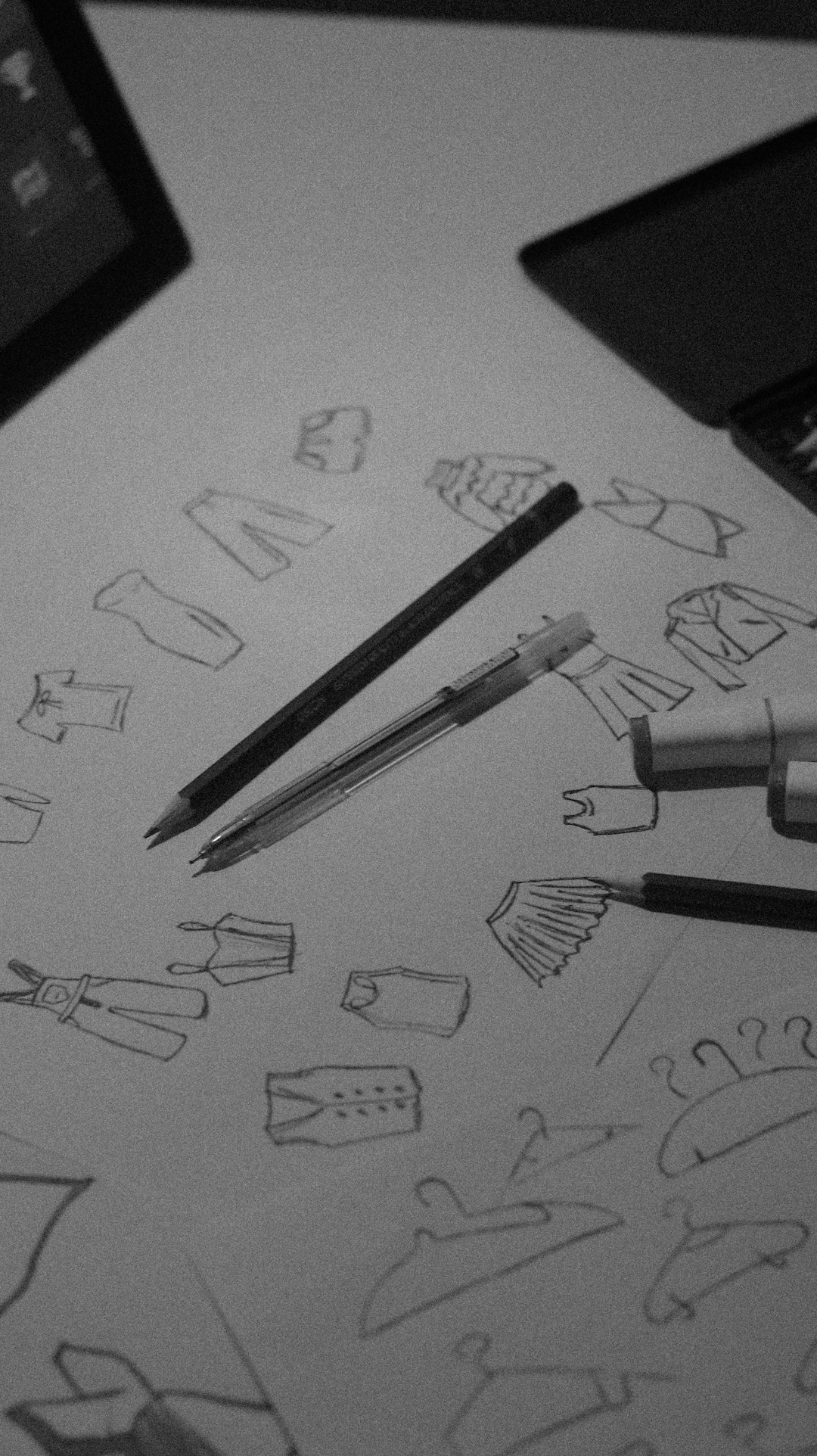 Sketches of clothing designs drawn on paper with pencils and a laptop nearby, suggesting a fashion design sketching session.