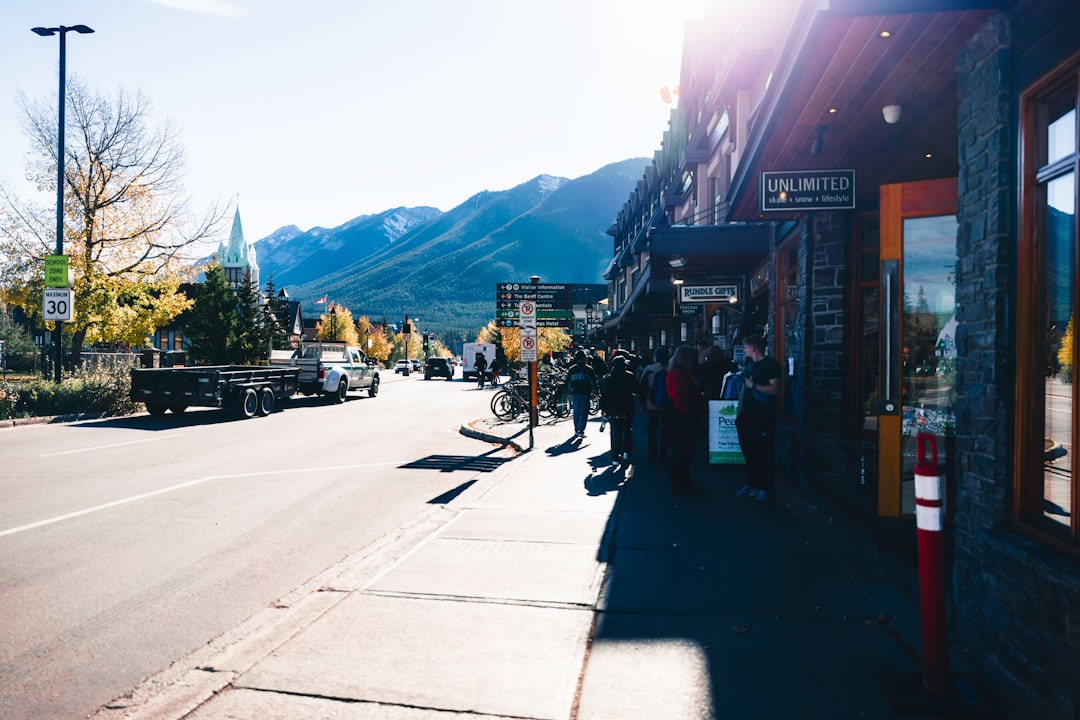 Sunlit alpine street with pedestrians outside shops and a mountain range in the background.
