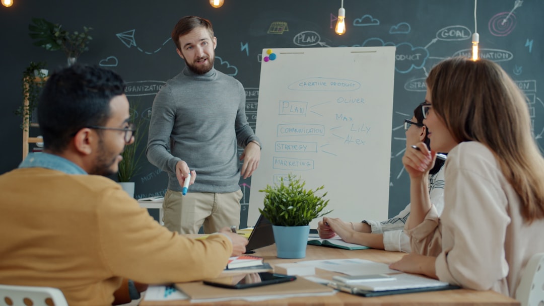 Team in a brainstorming session around a table with a whiteboard showing a workflow diagram and notes.