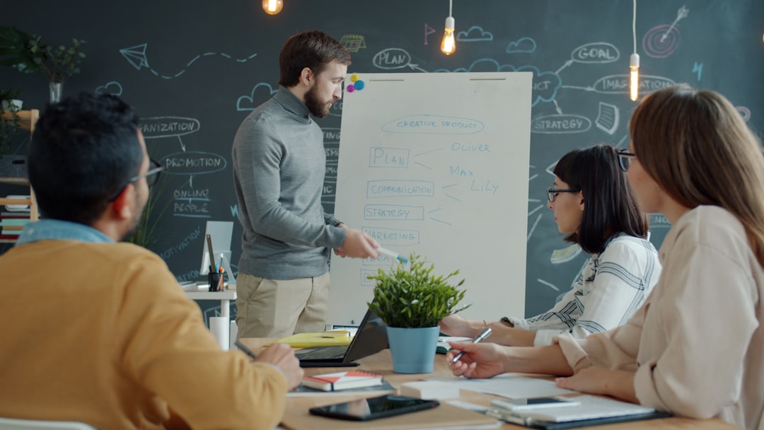 Four teammates in a meeting around a table, presenting ideas on a whiteboard with diagrams and flowcharts.
