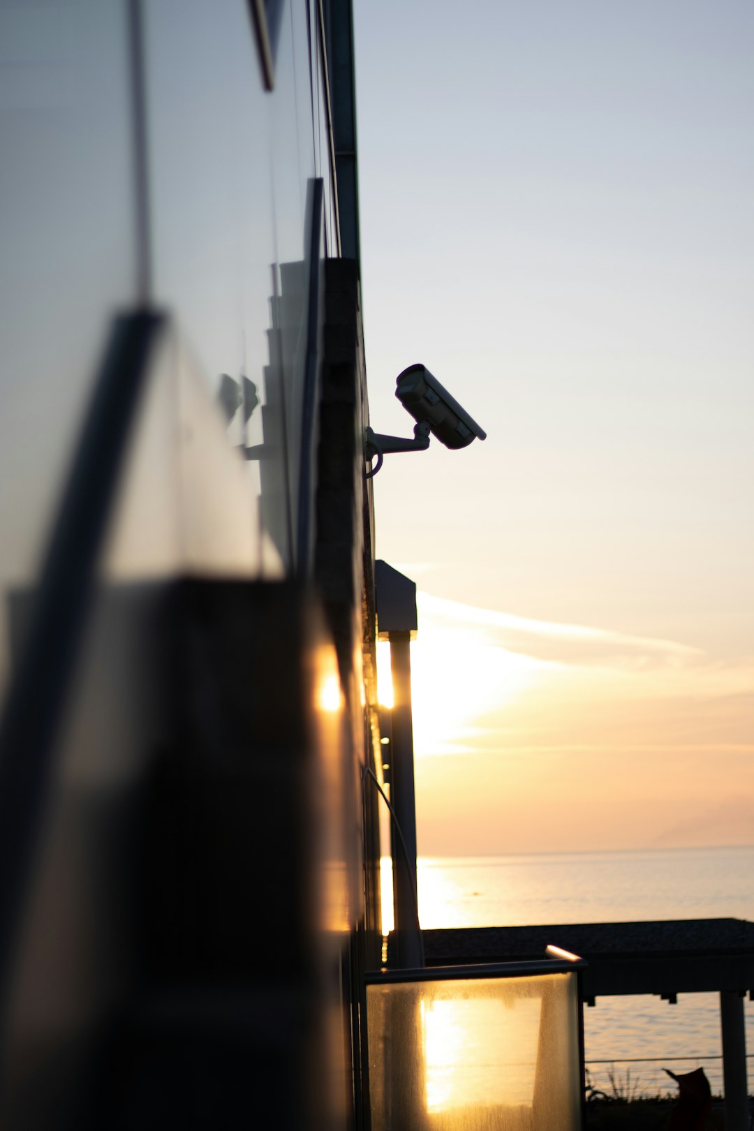 Security camera mounted on the side of a building with sunset reflecting on the water behind it.