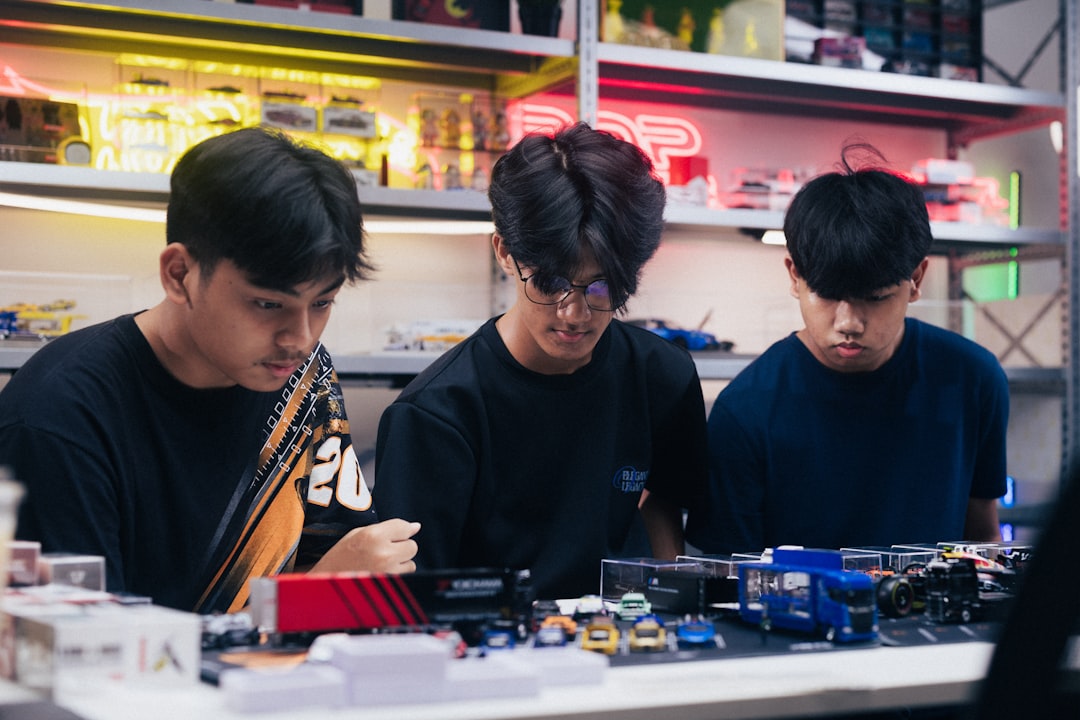 Three young men lean over a table of model cars in a hobby shop, focused on the miniature vehicles.