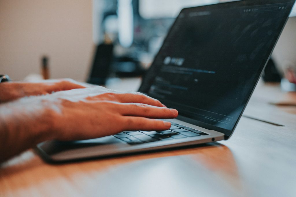 Hands typing on a laptop keyboard at a wooden desk.