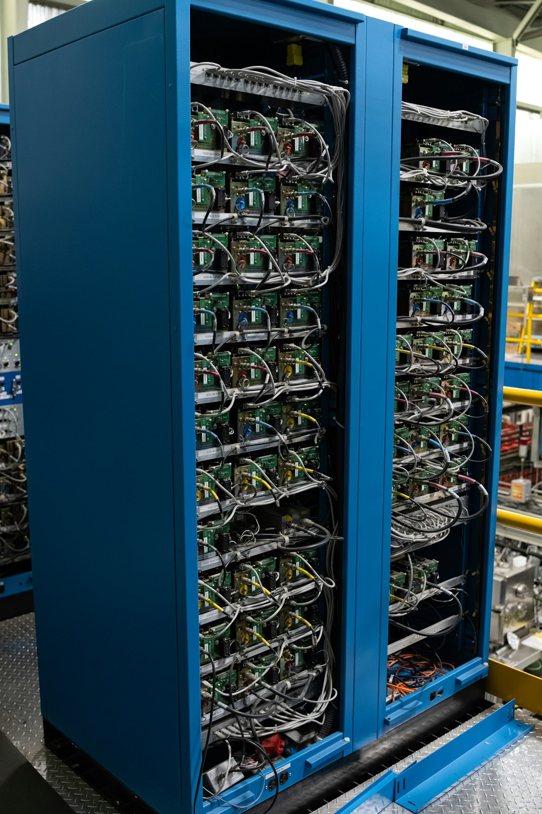 Blue equipment cabinet (server rack) with densely wired circuit boards and cables in an industrial setting, suggesting IT/telecom hardware installation.