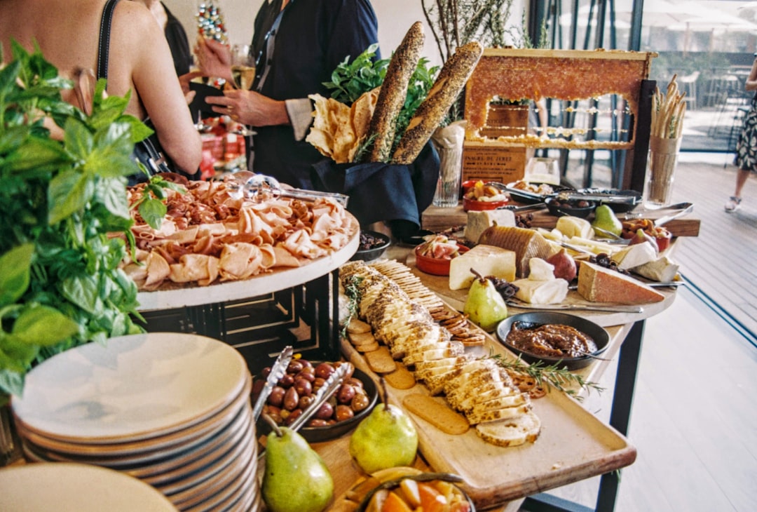 A large buffet table with sliced meats, cheeses, bread, olives, fruit, and condiments at a social event.