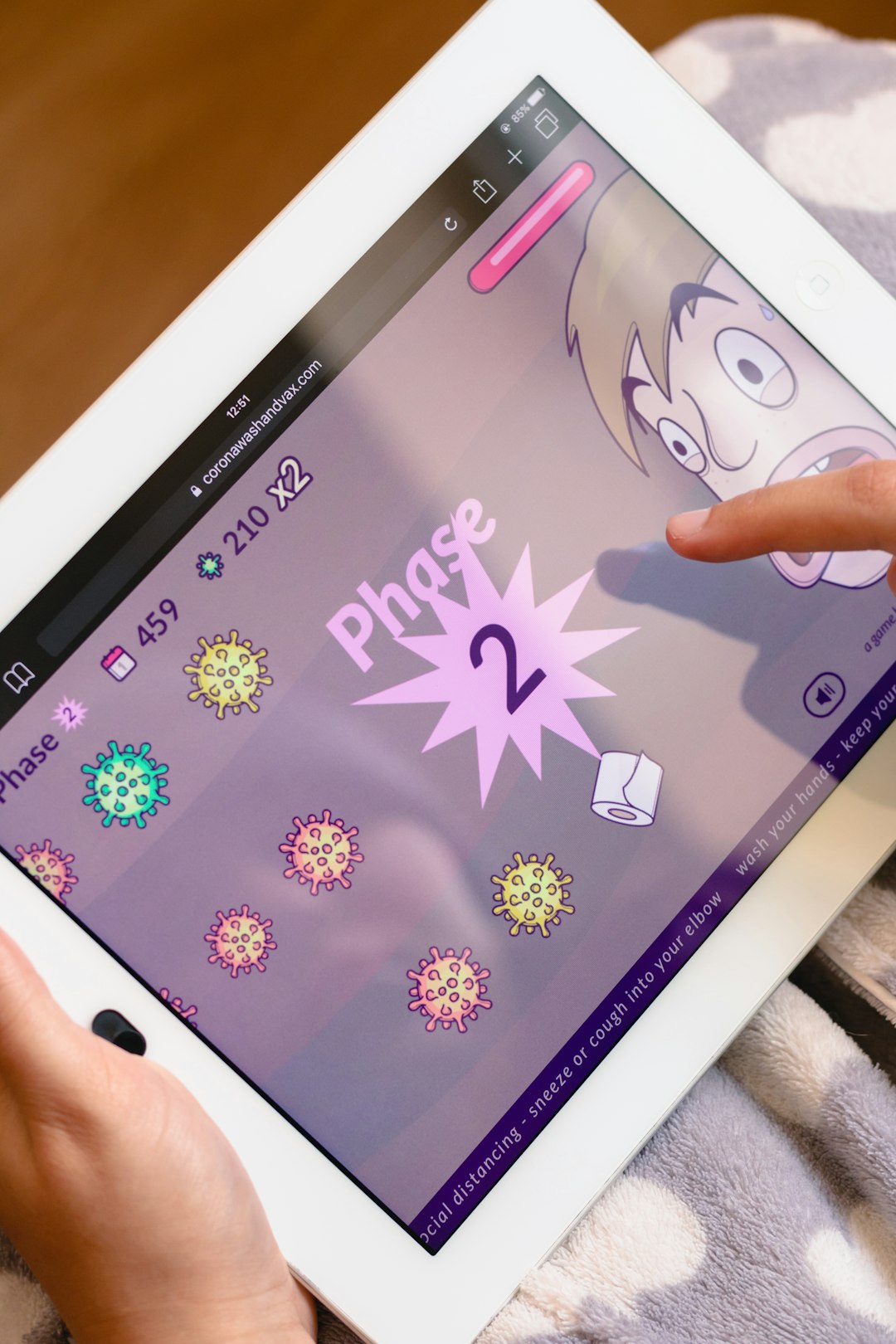 Tablet screen displaying a cartoon game with a pink ‘Phase 2’ burst and colorful virus icons.