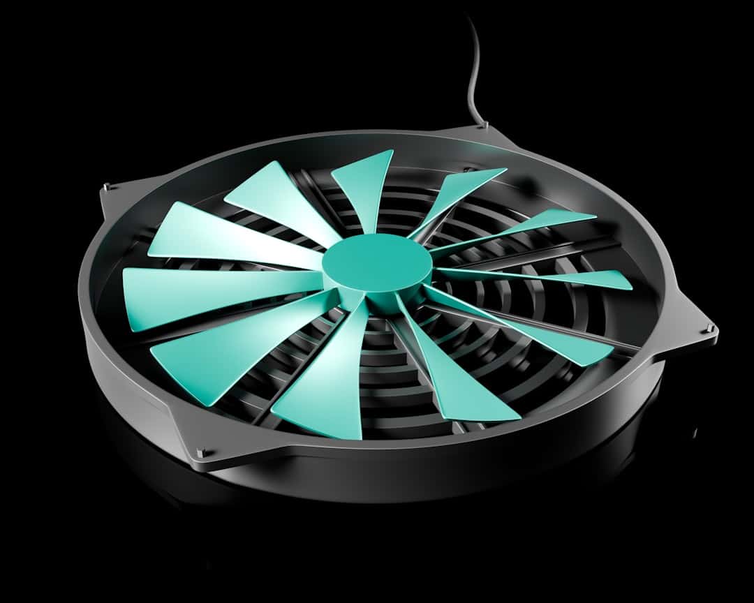 Teal computer cooling fan with mint-green blades inside a black circular housing on a black background, close-up view