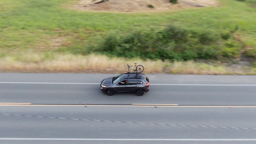 Black SUV with a bicycle mounted on roof rack driving on a paved highway beside a grassy embankment.