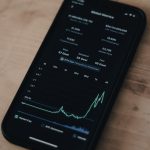 Smartphone screen showing a cryptocurrency market dashboard with a rising line chart and numeric stats on a dark UI.