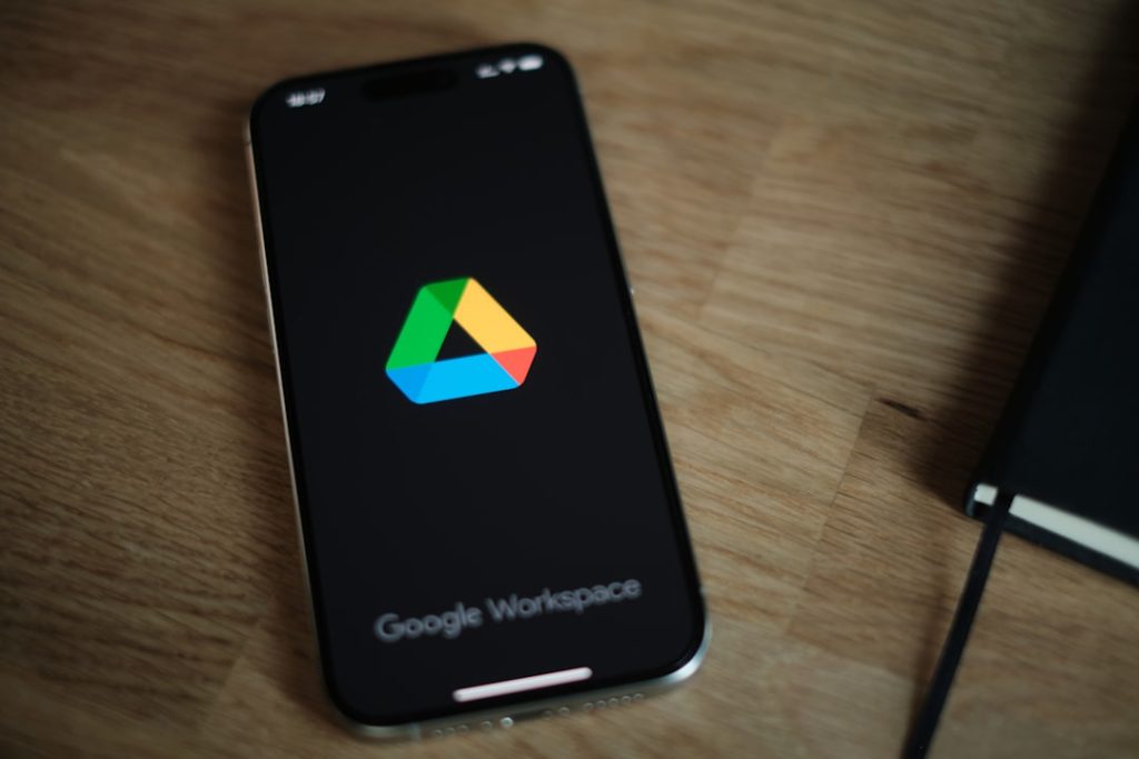 Smartphone on a wooden desk showing the Google Workspace logo on a dark screen from a slight angle.