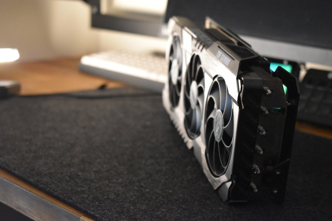 Graphics card with three cooling fans resting on a desk in front of a monitor and keyboard visible in the background.