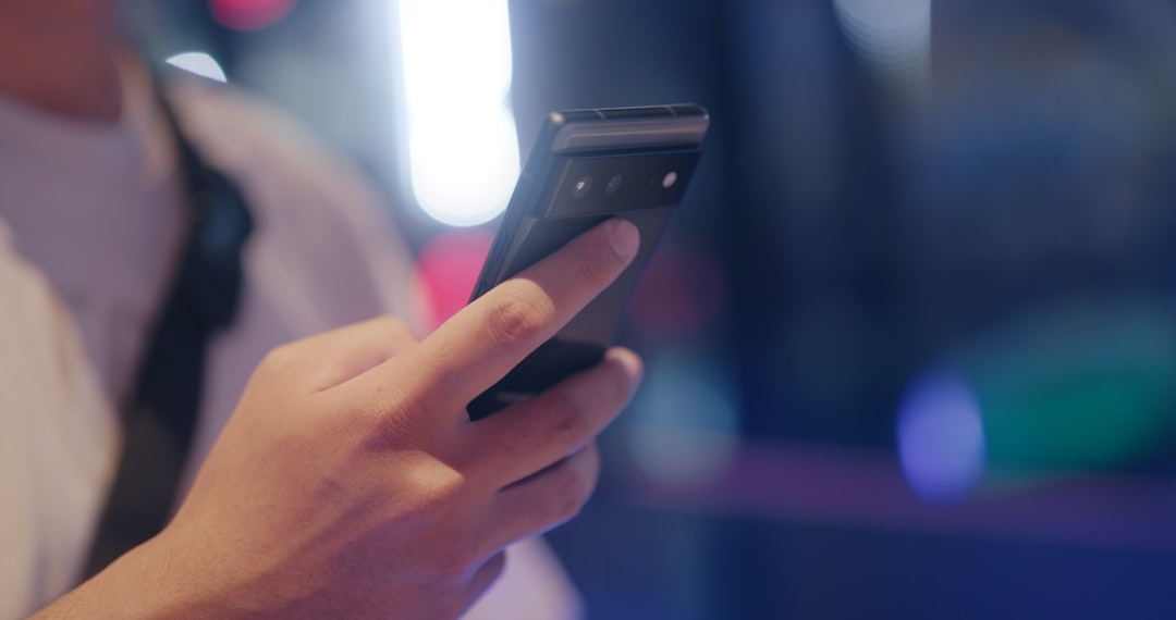 Person holding a black smartphone and tapping the screen in a dim, neon-lit setting.