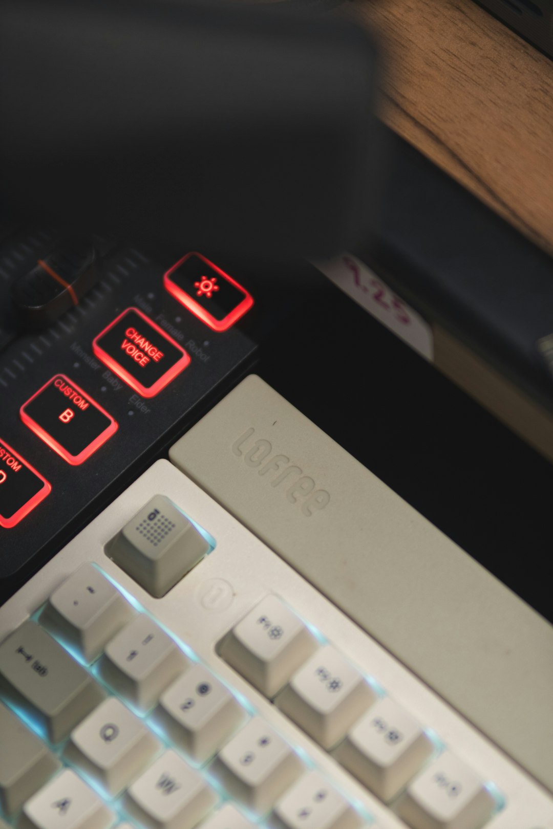 Close-up of a dark control panel with red glowing keys labeled 'Change Voice' and 'Custom B' beside a beige Lofree keyboard.