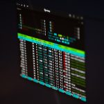 Computer monitor displaying a dark terminal with colorful stock data tables.
