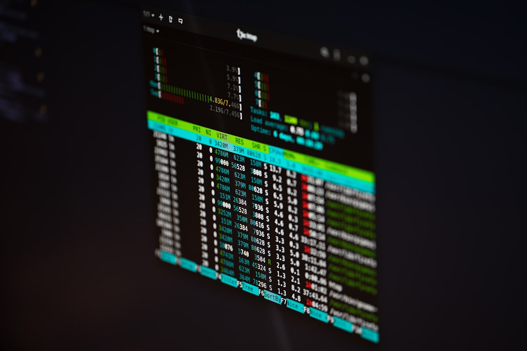 Close-up of a dark monitor displaying a colorful terminal window with rows of numbers and process columns (PRI, NI, VIRT, RES)./