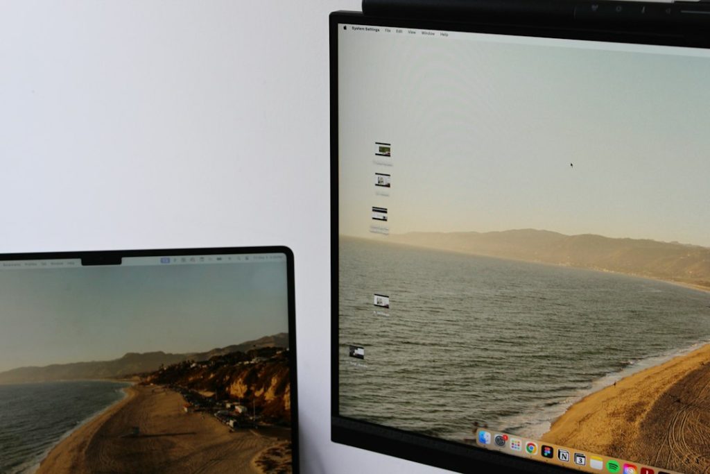 Two screens showing the same coastal wallpaper: a laptop on the left and a larger monitor on the right displaying a beach scene.