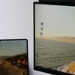 Two screens showing the same coastal wallpaper: a laptop on the left and a larger monitor on the right displaying a beach scene.