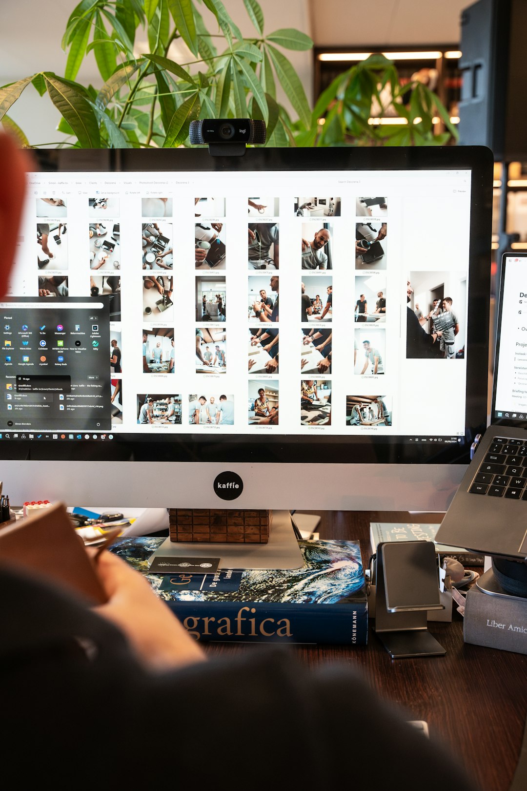 Desktop monitor showing a grid of thumbnail photos, with a small webcam perched on top and a plant in the background.