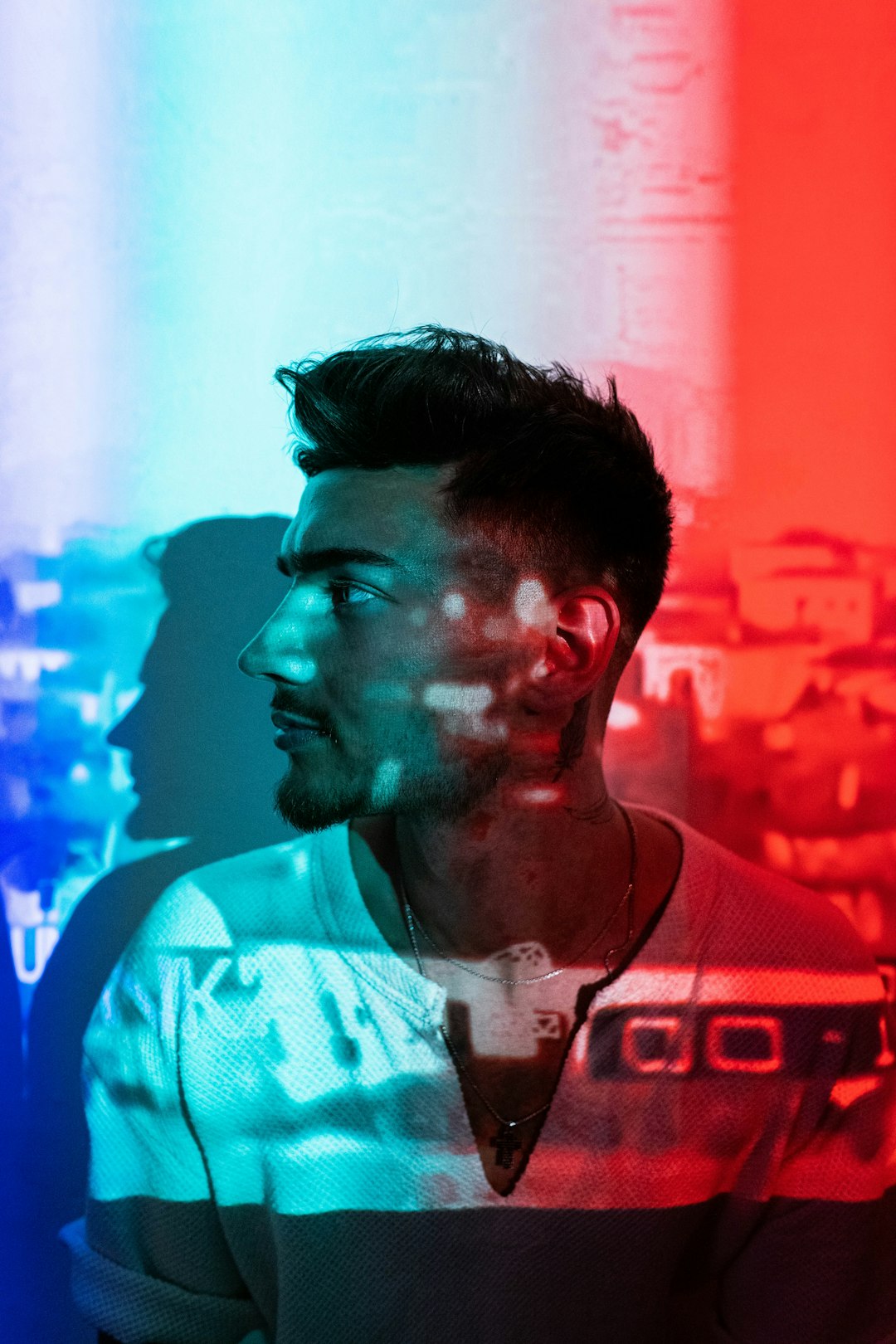 Side-profile of a young man with a short beard, lit by blue on the left and red on the right.