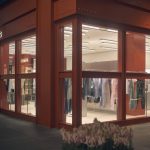 Acne Studios storefront at dusk with large glass windows showing clothing on display inside a red exterior storefront