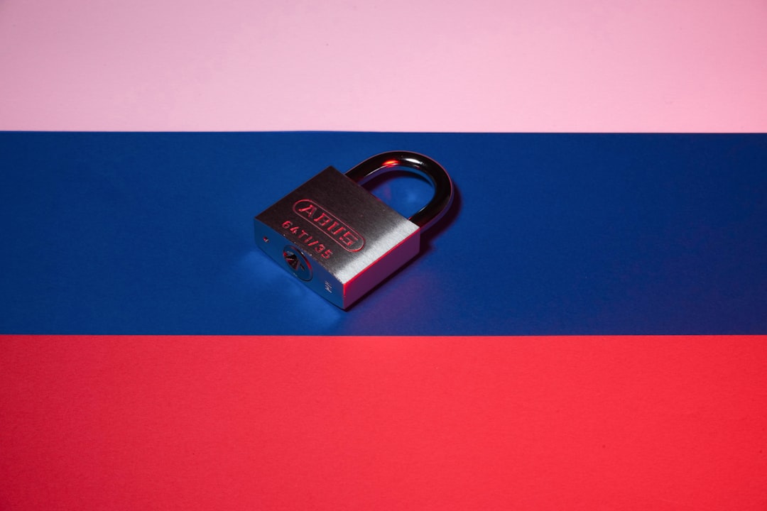ABUS padlock resting on a blue surface with pink above and red below the background.