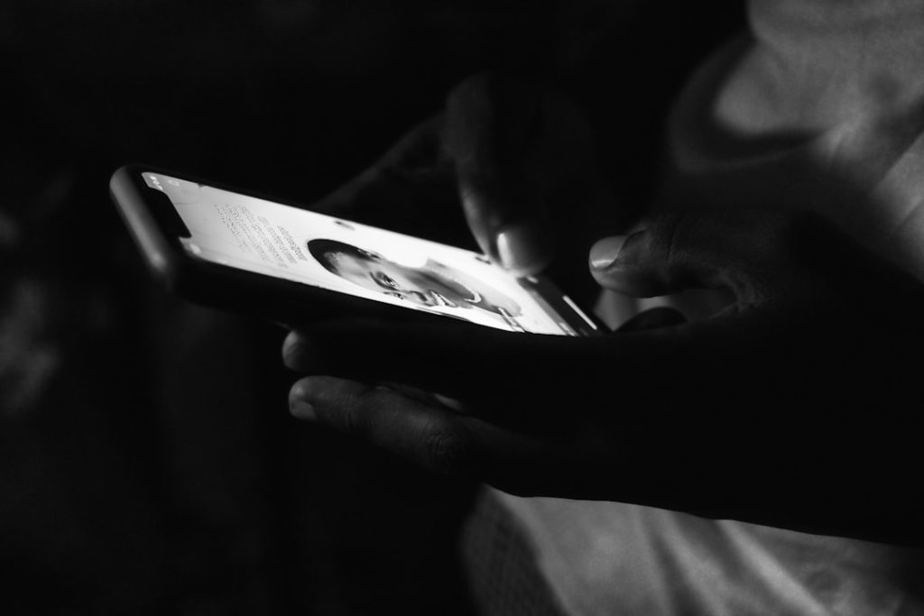 Hands holding a smartphone in low light, screen shows a text chat with a profile photo.