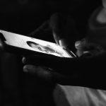 Hands holding a smartphone in low light, screen shows a text chat with a profile photo.
