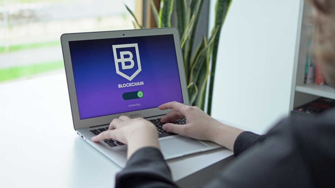 Person typing on a silver MacBook displaying a Blockchain logo with a loading bar that says 'connecting' on the screen.