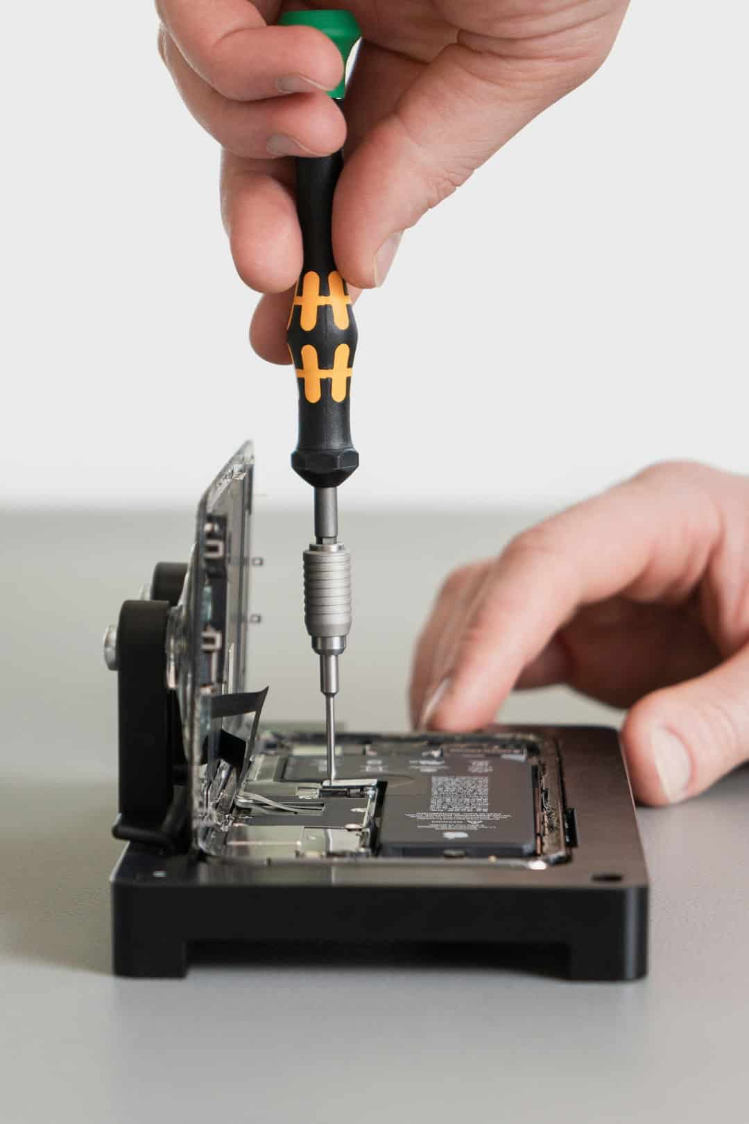 Hands use a precision screwdriver to work on the internal electronics of a small device.
