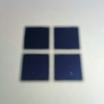Blurred photo of four dark blue square tiles arranged in a 2x2 grid on a light surface, with small star-like specks inside each tile.