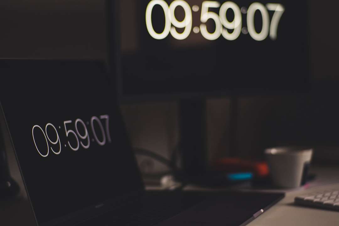 Desk setup with two screens displaying the large time 09:59:07; blurred coffee cup in the background.