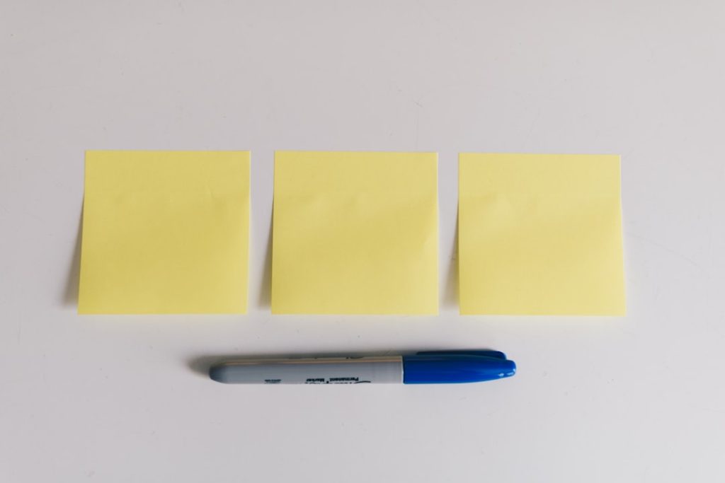 Three yellow sticky notes lined up on a white surface with a blue and gray marker beneath them.
