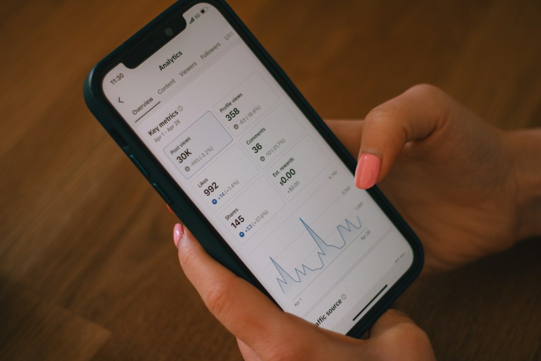 Close-up of hands holding a smartphone showing analytics dashboard with metrics and a line chart on screen.