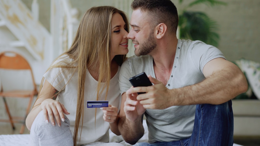 Couple sitting together, one holds a credit card while the other uses a smartphone for online shopping at home.