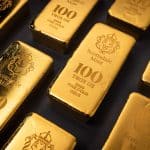 Gold bars stamped Scottsdale Mint, each reading 100 TROY OZ FINE GOLD, arranged on a dark surface.