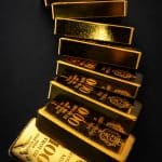 Diagonal stack of shiny gold bars on a dark background, angled in a twisting column.