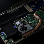 Open laptop with exposed motherboard, cooling fan, copper heat pipe, and battery
