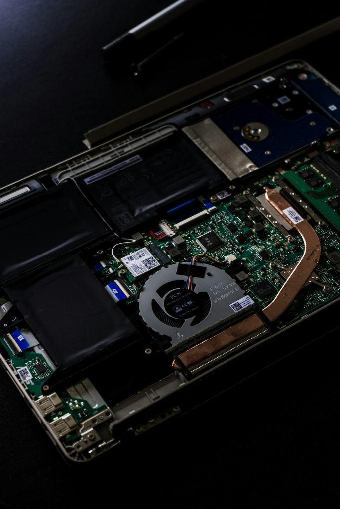 Open laptop with exposed motherboard, cooling fan, copper heat pipe, and battery
