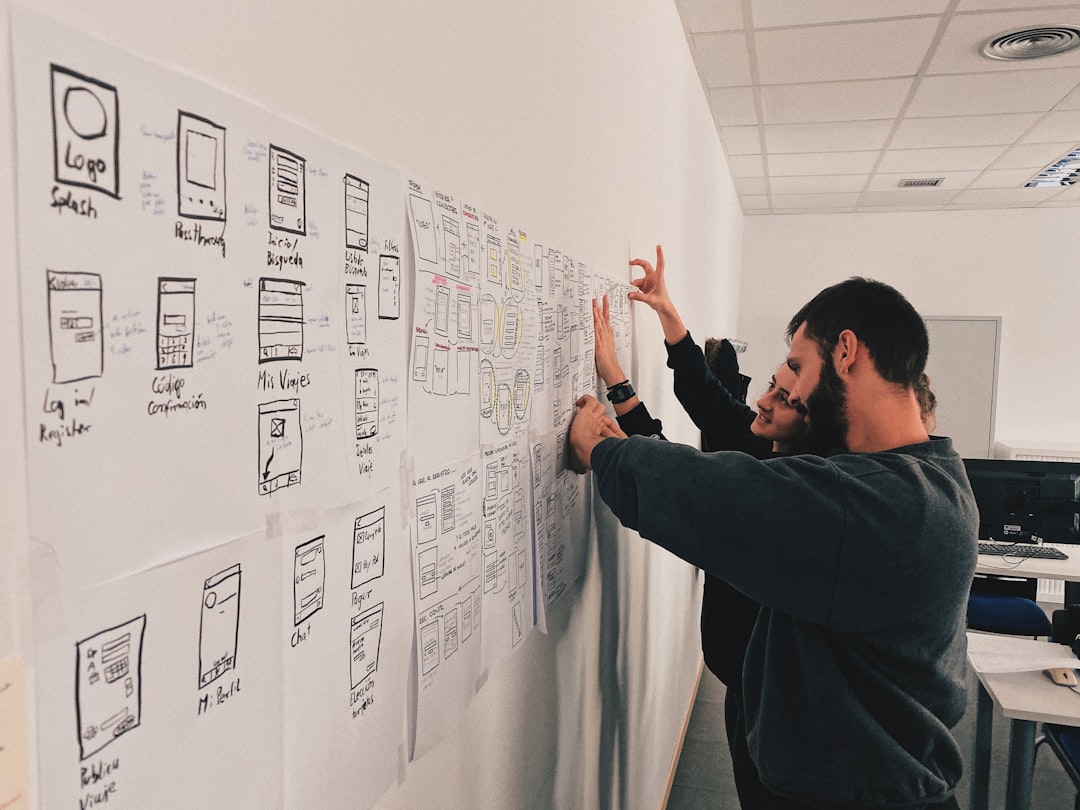 Team of designers taping up hand-drawn app wireframes on a white wall during a planning session.