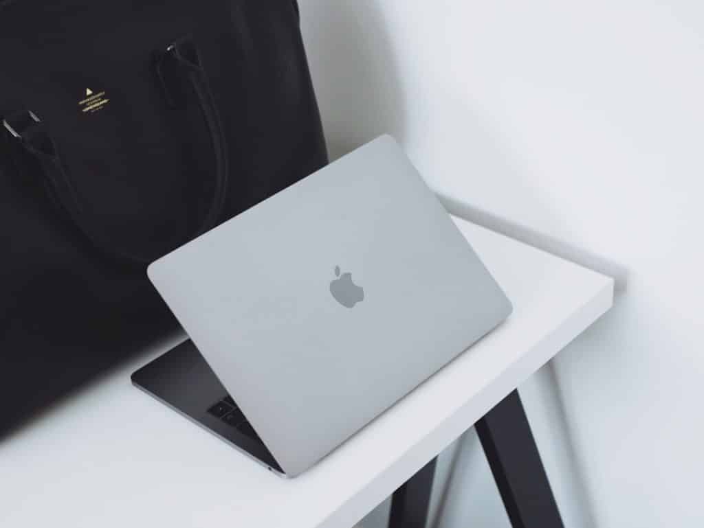Silver MacBook laptop resting on a white desk with a black bag nearby.