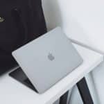 Silver MacBook laptop resting on a white desk with a black bag nearby.