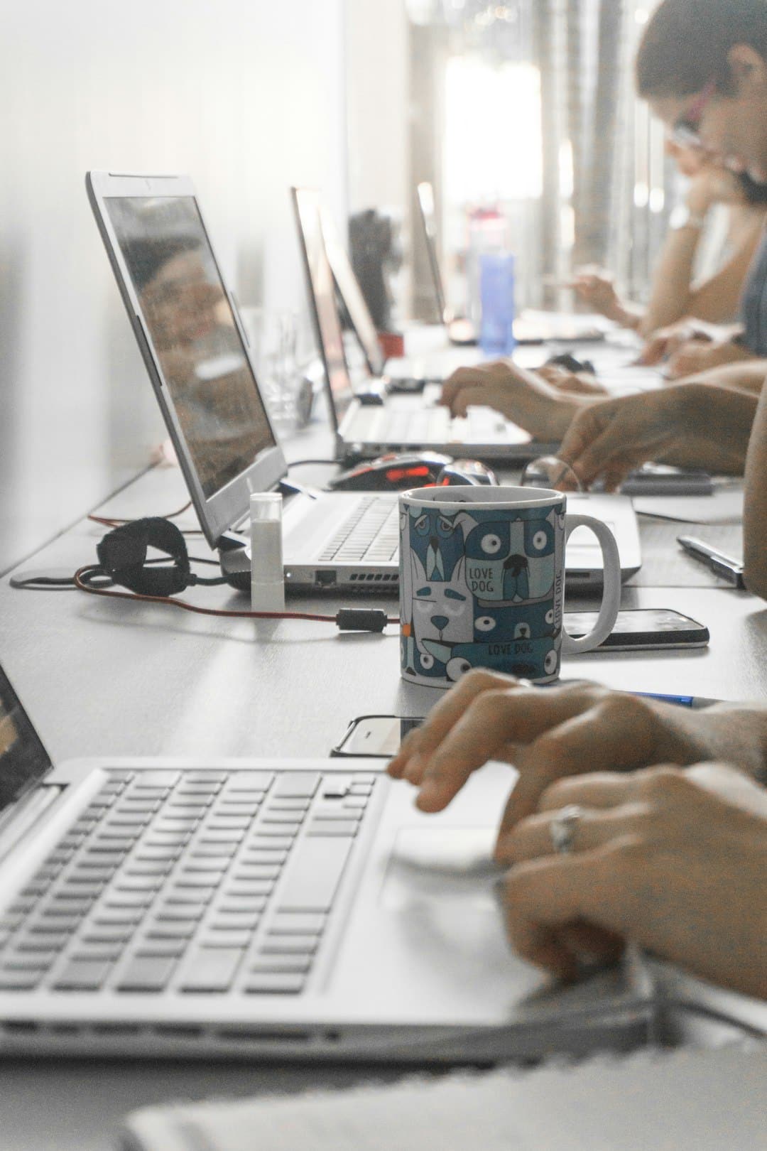 Row of laptops on a long desk with a blue patterned mug in the foreground as people type