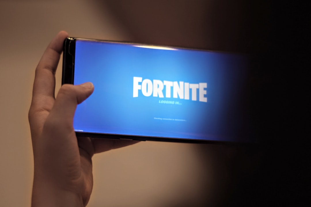 Close-up of a hand holding a smartphone in landscape mode showing the Fortnite loading screen in blue.